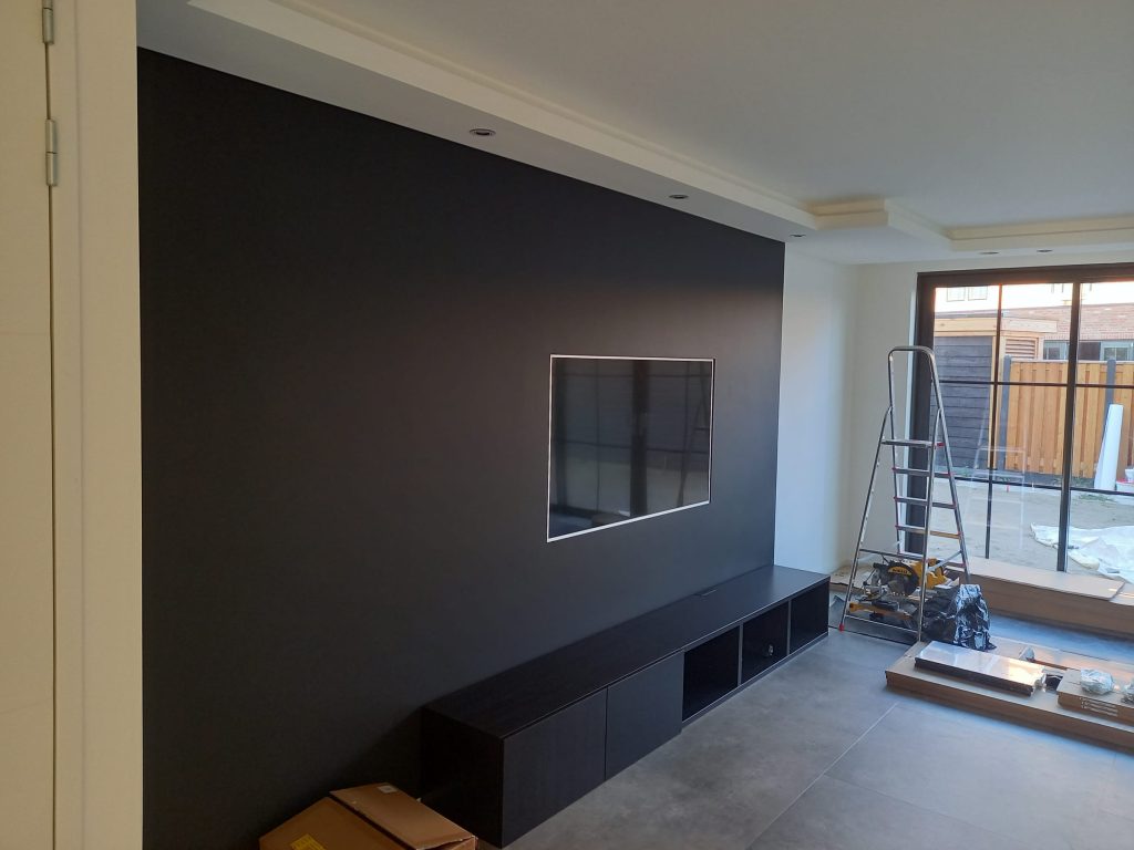 Woonkamer in afbouw met donkere wand en haardmeubel