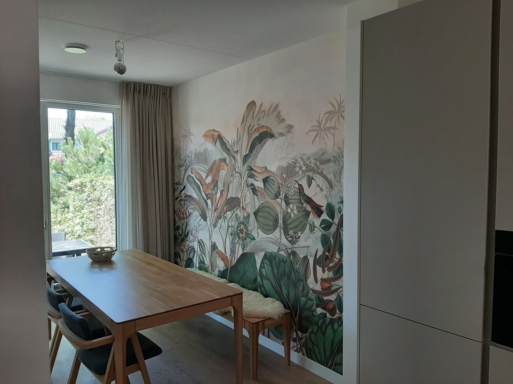 Eetkamer met fotobehang van planten en vogels naast een houten eettafel